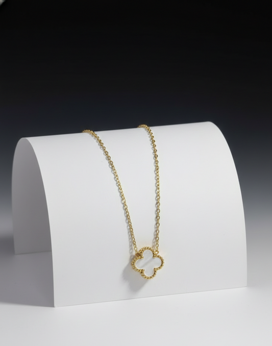Gold necklace with a clover-shaped pendant on a white stand against a dark background
