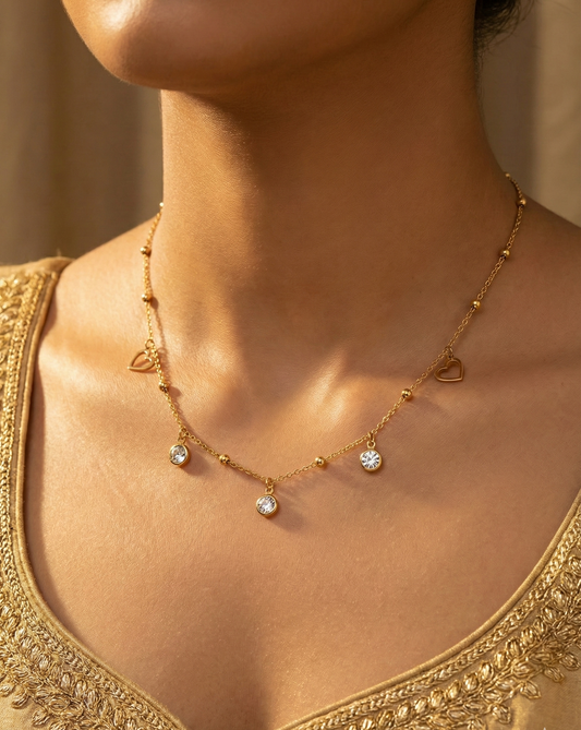 Gold necklace with heart and gemstone details worn by a person in a gold top.